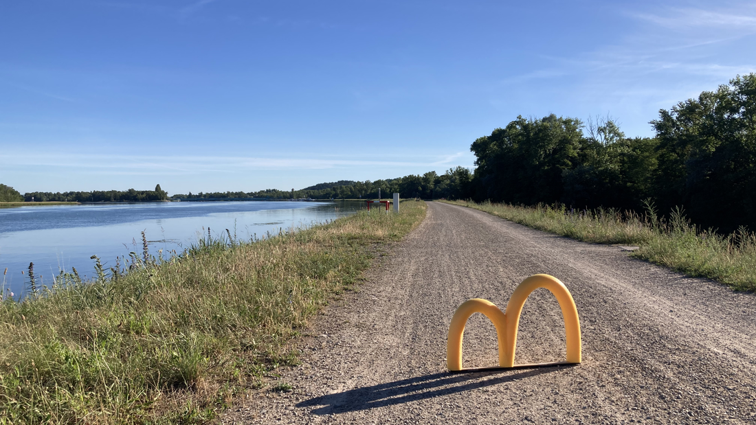 Gelbes "m" steht auf einem langen geraden, weit in die ferne verlaufenden Radweg