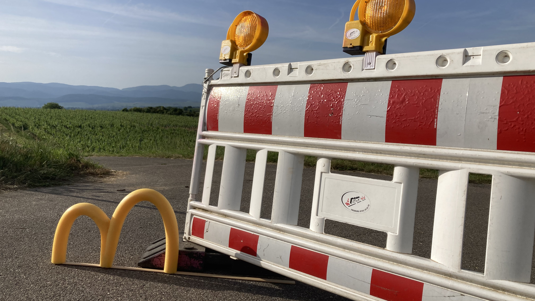 Gelbes "m" steht vor einem Absperrgitter an der Strasse