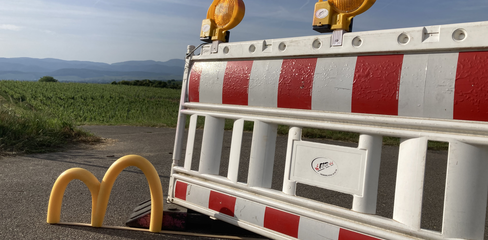 Gelbes "m" steht vor einem Absperrgitter an der Strasse