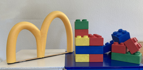 Gelbes "m" steht auf einem Tisch neben großen bunten Legosteinen